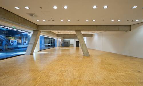 dynamicum Der Konferenzraum dynamicum ist unbestuhlt. Die Glastüren auf der linken Seite sind zum atrium hin geöffnet. In der Mitte des Raumes befindet sich ein Raumteiler aus Beton.