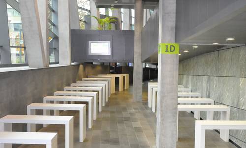 Foyer 1.08 Weiße Stehtische wurden im Foyer 1.08 aufgebaut. Auf dem linken Bildrand erkennt man die Außenfassade, die zur Erich-Ollenhauer-Promenade zeigt. Auf der rechten Seite befindet sich die rechte Außenwand des großen Saals spectrum, an der die Rampe bis in die dritte Ebene des Hauses führt.