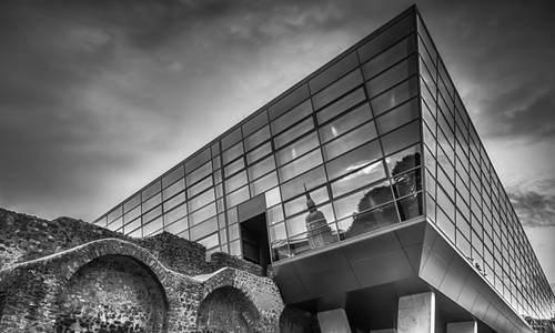Copyright: Lothar Keuch Eine schwarz-weiße Ansicht von der rechten Ecke des darmstadtiums und der Stadtmauer, von der Erich-Ollenhauer-Promenade aufgenommen. In den Glasscheiben spiegelt sich das Hessische Landesmuseum.