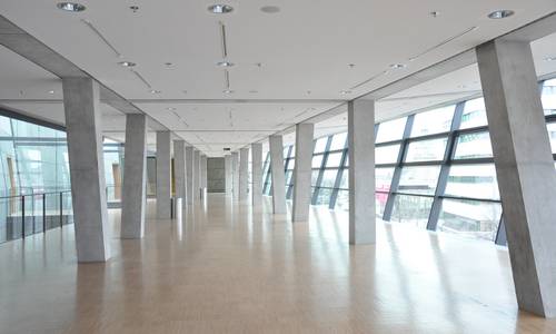 Foyer 3.11 Blick durch den mittleren Bereich des Foyers 3.11. Im Foyer befindet sich kein Mobilar- sichtbar sind nur die Betonpfeiler, die das gesamte Foyer säumen. Man erkennt die Schrägen der Fenster auf der rechten Seite. Auf der linken Seite befinden sich die Außenwände des großen Saals.