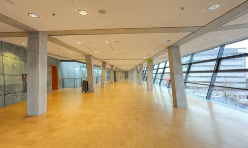 Foyer 3.11 Blick durch den mittleren Bereich des Foyers 3.11. Im Foyer befindet sich kein Mobilar- sichtbar sind nur die Betonpfeiler, die das gesamte Foyer säumen. Man erkennt die Schrägen der Fenster auf der rechten Seite. Auf der linken Seite befinden sich die Außenwände des großen Saals.